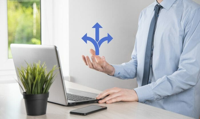 Male hand holding icon with three directions icon on blue background.n doubt, having to choose between three different choices indicated by arrows pointing in opposite direction concept. three ways to choose